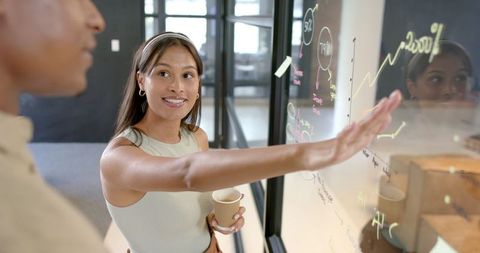 Businesswoman Explains Data to Colleague on Office Whiteboard