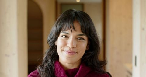 Smiling woman in cozy wooden hallway wearing red sweater