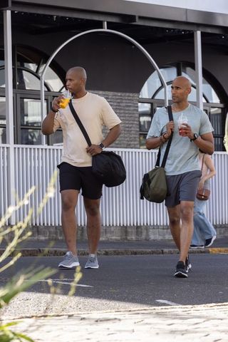 African american men walking with duffel bags drinking iced drinks on urban sidewalk