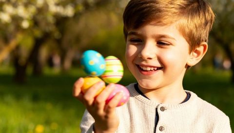 Smiling boy holding colorful easter eggs in sunlit park orchard, spring family moment