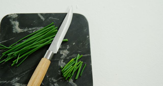 Fresh green chives on a black marble board with a sharp kitchen knife. Suitable for illustrating cooking, recipe creation, fresh ingredients, or kitchen tool designs. Perfect for food blogs, culinary websites, cookbooks, or kitchenware product advertisements.