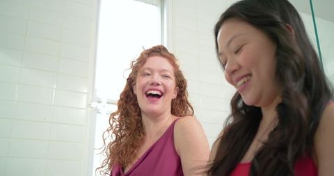 Laughing diverse women sharing candid moment in bright tiled bathroom with natural light