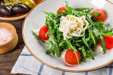 Arugula salad featuring burrata cheese and peeled cherry tomatoes on rustic plate