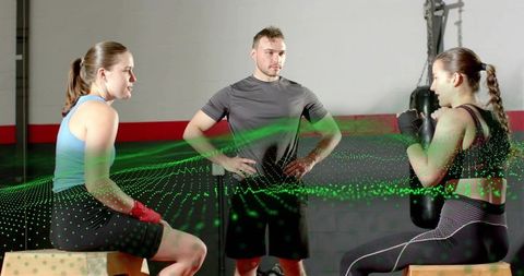 Coach coaching two women boxers in gym with digital holographic grid overlay