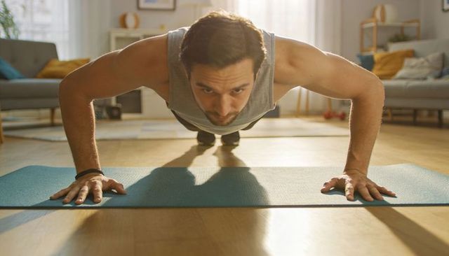 Man doing push-up on blue mat in sunlit living room, home workout fitness lifestyle toning