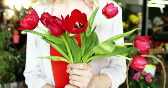 Female florist holding bunch of red flower in flower shop