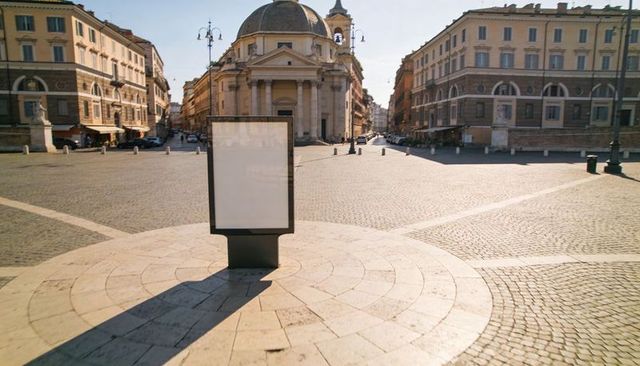 Standing blank advertising panel on sunlit cobblestone piazza with domed neoclassical church