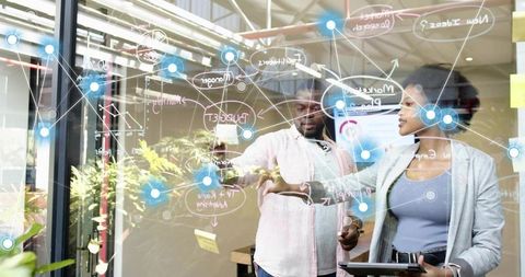 Diverse tech team collaborating on interactive glass wall strategy map with tablet