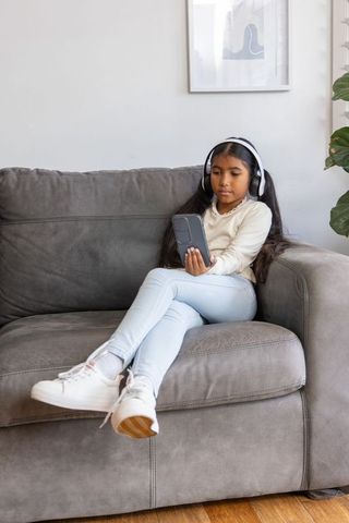 Young asian girl listening to music and using smartphone while relaxing on gray sofa