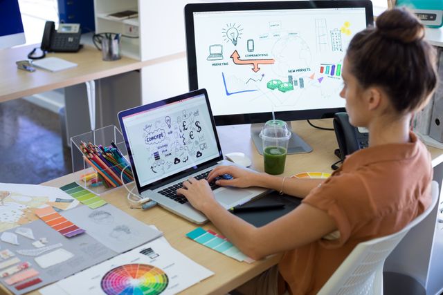Female executive engaged in graphic design work on laptop at her desk in a modern office. Suitable for presentations on workplace environments, professional work culture, creativity in business, and remote design work.
