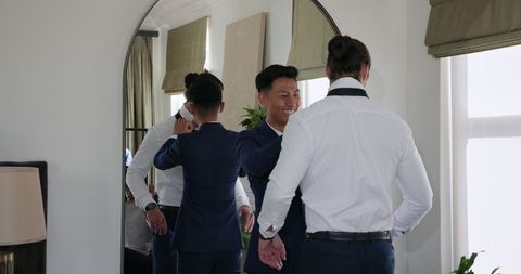 Groom and best man preparing for wedding in front of mirror