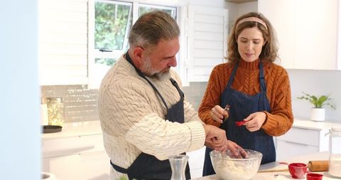 Middle-aged couple baking in bright home kitchen kneading dough adding vanilla extract
