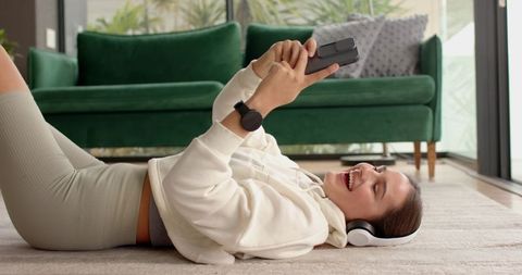Woman Relaxing with Smartphone and Headphones on Cozy Rug