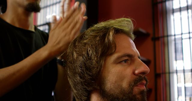 A Caucasian middle-aged man is getting his hair styled by a barber, with copy space. Capturing a moment of personal grooming, the image reflects the everyday activity in a barbershop.