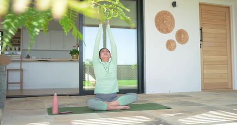 Sunlit morning yoga on patio with mid adult asian woman stretching, practicing mindful breathing