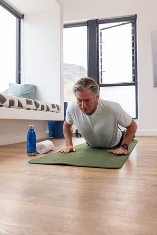 Mature man performing push-up on green mat in sunlit modern home workout routine
