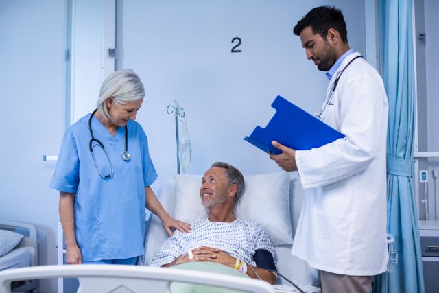 Doctor and nurse are attending to an elderly male patient in a hospital room. The patient is lying in bed, smiling, while the nurse places a comforting hand on his shoulder and the doctor reviews medical notes on a clipboard. This image can be used for healthcare, medical services, patient care, hospital advertisements, and health-related articles.