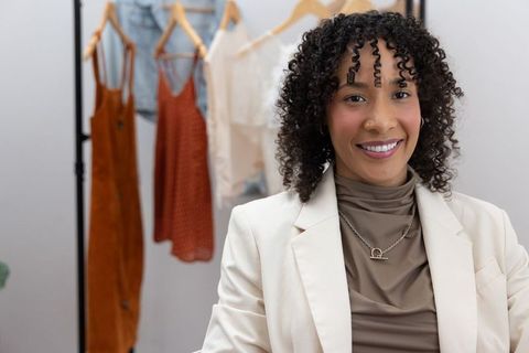 Smiling african american boutique owner presenting curated wardrobe in chic cream blazer