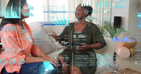 Two women discussing financial analytics with holographic data overlays on sofa