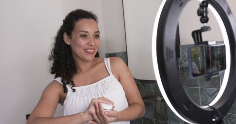 African american influencer filming skincare routine and applying cream with ring light