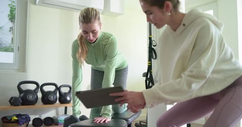 Female trainer coaching home strength workout using tablet on bench with kettlebells