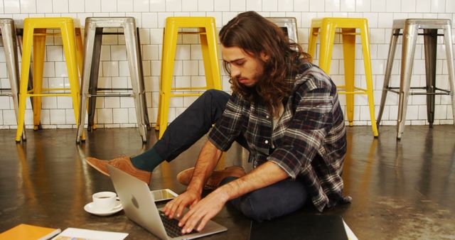 Young man working on laptop while sitting on floor in modern cafe - Download Free Stock Images Pikwizard.com