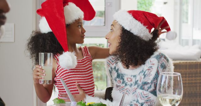 Happy african american mother and daughter wearing santa hats and celebrating in kitchen. family christmas time and festivity together at home.