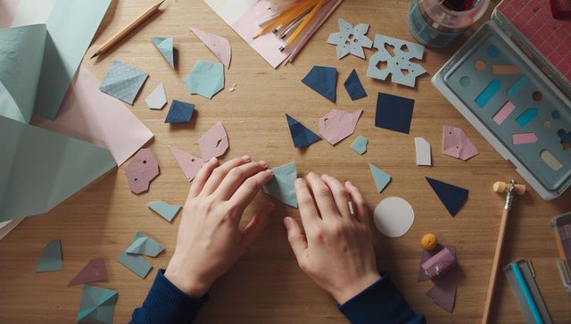Creative hands crafting origami with pastel paper cutouts on wooden desk