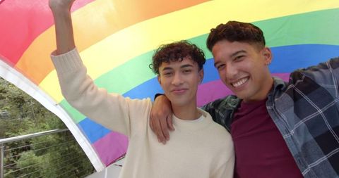 Hispanic Friends Celebrating Pride with Rainbow Flag Outdoors
