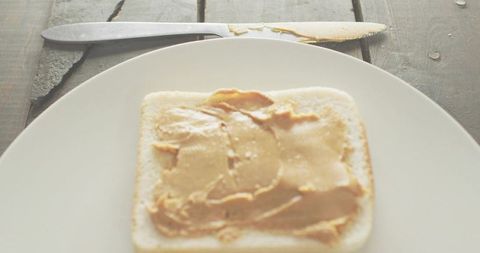 Spreading Peanut Butter on White Bread Overhead Rustic Wooden Table Morning Light