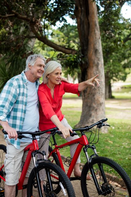 Senior couple standing with bicycle in park on a sunny day