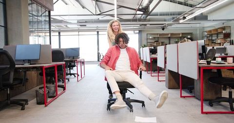 Colleagues having fun spinning on chairs in modern office workspace