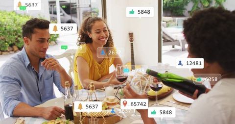 Smiling friends sharing wine at sunlit dining table with social media engagement icons