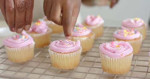 Senior Woman and Teenage Girl Decorating Pink-Frosted Cupcakes with Sprinkles on Cooling Rack