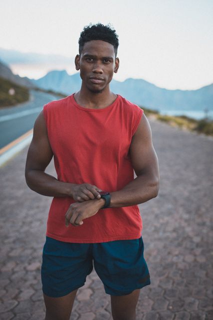 Fit african american man exercising outdoors on coastal road checking smartwatch. healthy outdoor lifestyle fitness training.
