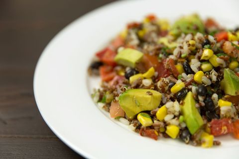Serving colorful quinoa, black bean, corn and avocado salad on white plate for healthy meal