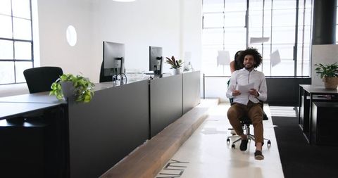 Colleagues enjoying office chair ride in modern workspace