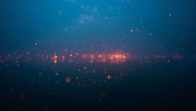 Glowing amber bokeh drifting across teal navy gradient with luminous orbs and soft grain