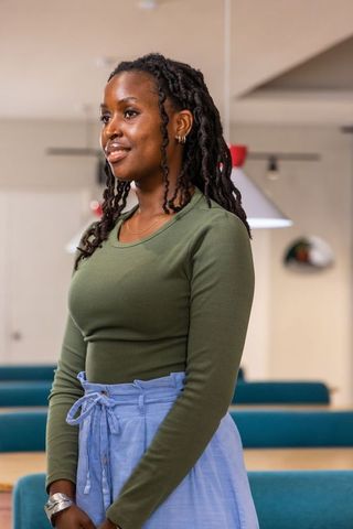 African american woman standing in coworking space wearing olive top and blue pants