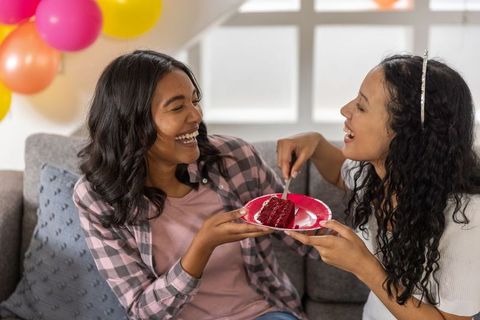 Diverse friends laughing sharing cake on sofa during birthday celebration