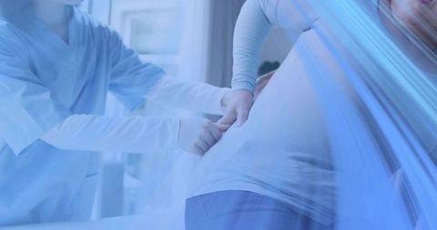 Nurse palpating pregnant abdomen during prenatal exam in bright clinical environment