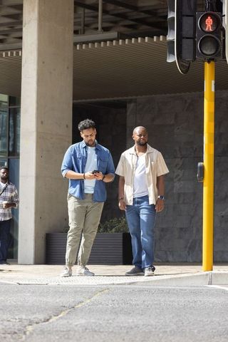 Two african men standing at crosswalk checking smartphone under city overhang