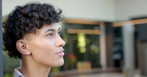 Young Man Looking Up in Modern Atrium, Curly Hair, Cross Earring, Thoughtful Profile
