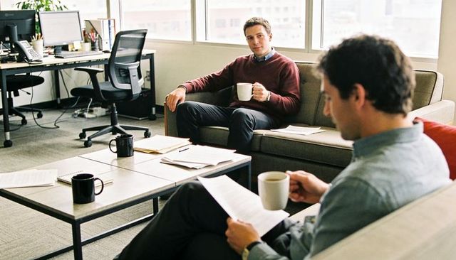 Colleagues sharing coffee and reviewing documents in modern office lounge