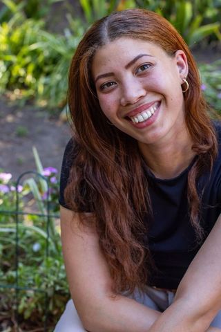 Smiling african american woman sitting in garden among blooms, outdoor lifestyle portrait