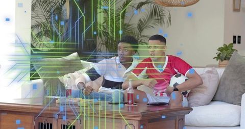 Friends watching soccer match on couch holding ball, reacting with futuristic digital overlay
