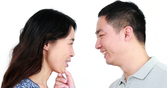 An Asian man and woman are facing each other with joyful expressions, with copy space. Their smiles and eye contact suggest a moment of happiness and connection.
