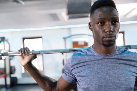 Man performing barbell squat across shoulders in gym wearing heather-blue shirt