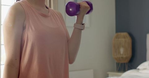 Woman exercising indoors with dumbbell in modern bedroom setting