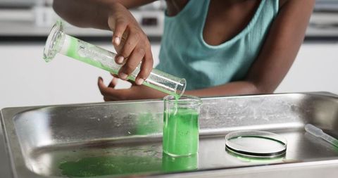 Student pouring bright green solution from graduated cylinder into beaker during experiment